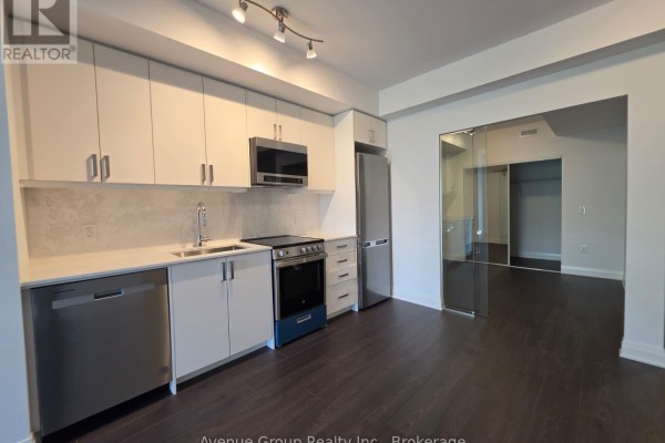 View of the kitchen and open-concept living space with dark hardwood floors and mirrored sliding doors. - 409 - 700 Sheppard Avenue W, Toronto