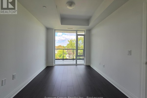 Empty room with dark hardwood floors and a large sliding glass door leading to a balcony with a green view. - 409 - 700 Sheppard Avenue W, Toronto