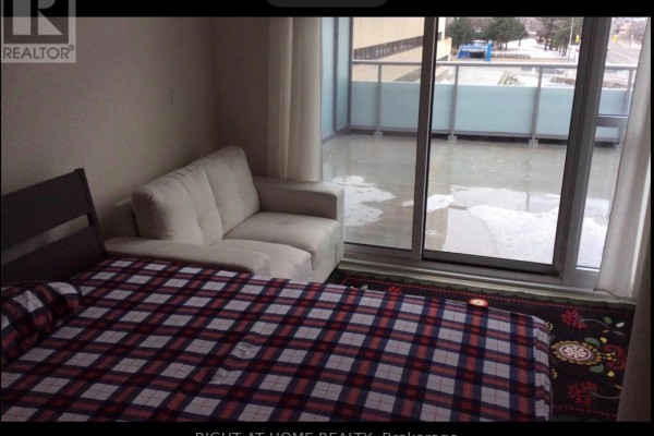 Bedroom with a white sofa, plaid blanket on a bed, and a balcony visible through glass doors. - 409 - 88 Sheppard Avenue E, Toronto