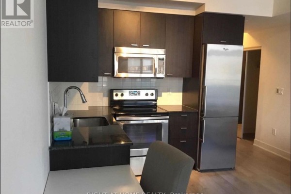 Kitchen with dark wood cabinets, stainless steel appliances including a refrigerator and microwave, and a granite countertop. - 409 - 88 Sheppard Avenue E, Toronto