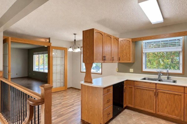 Kitchen with light wood cabinets, white countertops, a sink, and a view into a living room. - 409 11th Avenue S, Swan River