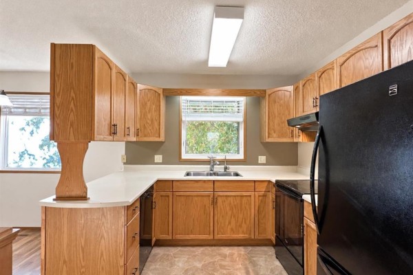 Kitchen with light wood cabinets, white countertops, a double sink, and a black refrigerator and stove. - 409 11th Avenue S, Swan River