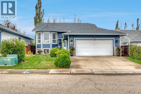 Front exterior of a blue house with a double garage and a well-maintained lawn. - 409 Strathford Bay, Strathmore