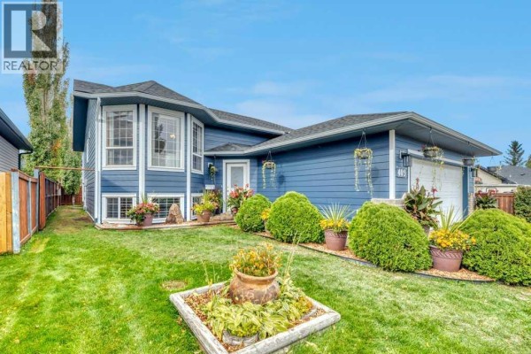 Front exterior of a blue house with bay windows, porch, and landscaped garden. - 409 Strathford Bay, Strathmore
