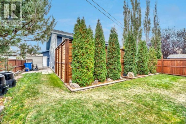 Backyard with a green lawn, tall evergreen trees, and a modern wooden fence. - 409 Strathford Bay, Strathmore