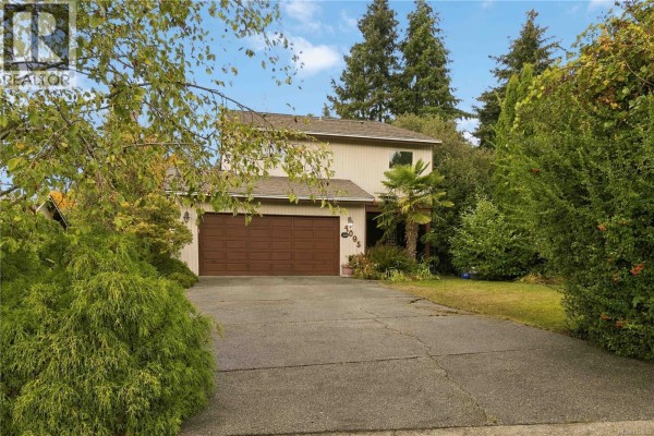 View of the beige house facade with a driveway and surrounding green foliage. - 4095 Beam Cres, Saanich