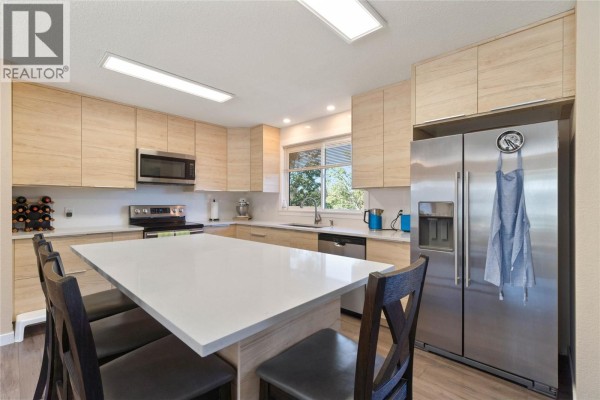 Kitchen island with seating, stainless steel refrigerator, and light wood cabinetry. - 41 Breccia Drive, Logan Lake