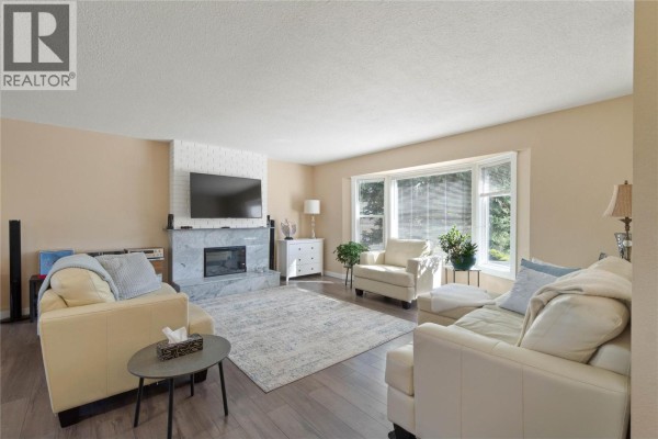 Living room with cream sofas, marble fireplace, large bay window, and light wood flooring. - 41 Breccia Drive, Logan Lake