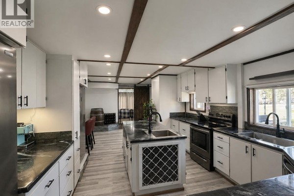 Another view of the kitchen highlighting the island, appliances, cabinetry, and a doorway to a living area. - 41 Cedar Street, Valemount