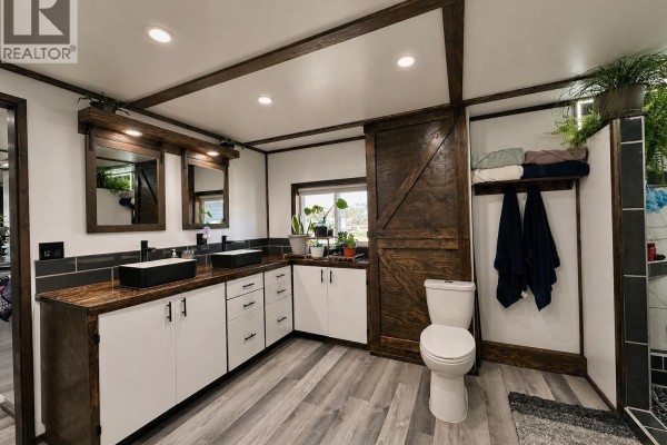 Bathroom with dual sinks, wooden countertops, toilet, sliding barn door, and walk-in shower with tiled walls. - 41 Cedar Street, Valemount