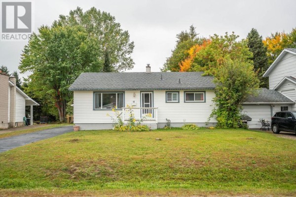 Front view of a white bungalow with a green lawn and mature trees in the background. - 41 Centre St, Sault Ste  Marie