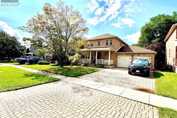 Street view of a two-story brick house with a covered porch, double garage, and paved driveway. - 41 David Street, Ingersoll