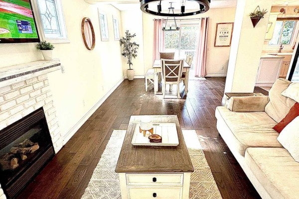 Living room with dark wood floors, a white brick fireplace, and a dining area with a table. - 41 David Street, Ingersoll
