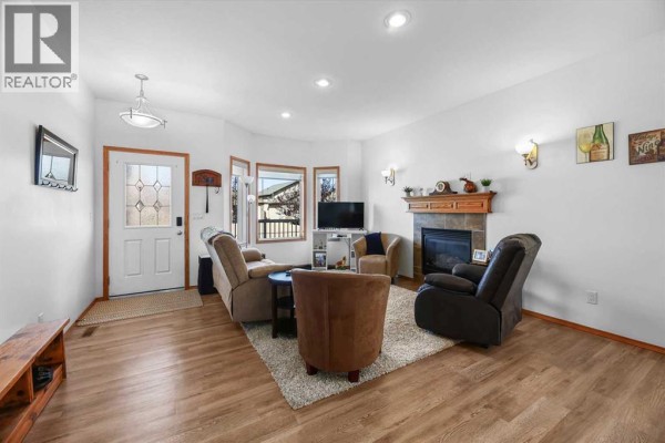 Living room with a gas fireplace, bay window, and tan flooring, furnished with sofas and chairs. - 41 Ebony Street, Lacombe