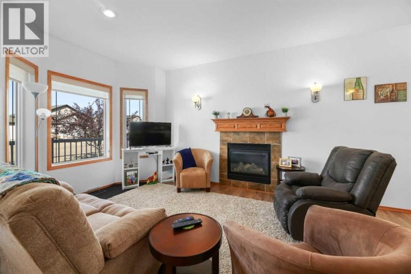 Living room facing the fireplace and window, furnished with a couch, chairs, and a plush rug. - 41 Ebony Street, Lacombe