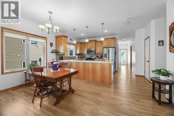 Open concept dining and kitchen area with light wood cabinetry, stainless steel appliances, and a wooden dining set. - 41 Ebony Street, Lacombe