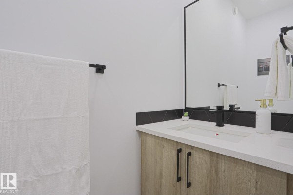 A modern bathroom vanity with a light wood cabinet, white countertop, and black fixtures. - 41 Elko Bn, St  Albert