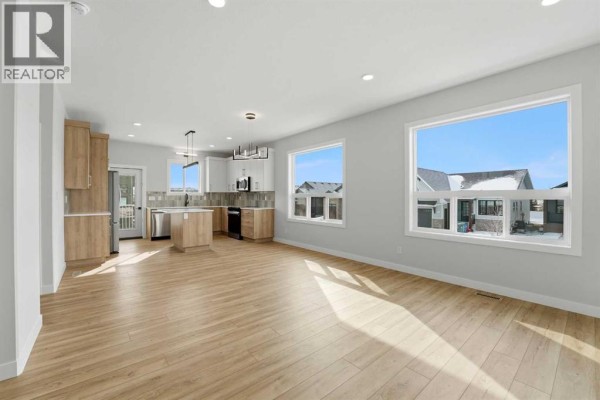 Open-concept living area with light wood floors, large windows, and a modern kitchen. - 41 Emmett Crescent, Red Deer