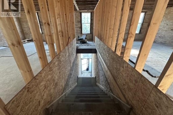 Interior view of unfinished upper floor with wooden framing, stairs, and windows. - 41 High Street W, Moose Jaw