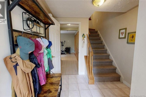 Foyer with beige tile floor, carpeted stairs, and coat rack with hanging clothes. - 41 Hillsview Crescent, Rothesay