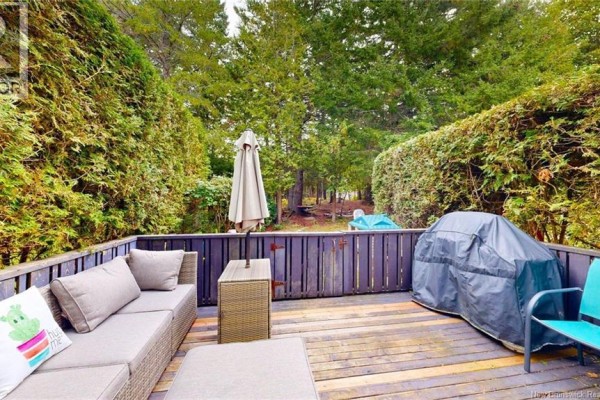 Wooden backyard deck with outdoor furniture, grill, and surrounded by lush greenery. - 41 Hillsview Crescent, Rothesay