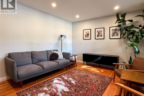 Living room with a grey sofa, patterned rug, wooden floors, and artwork on the wall. - 41 Motherwell Crescent, Regina