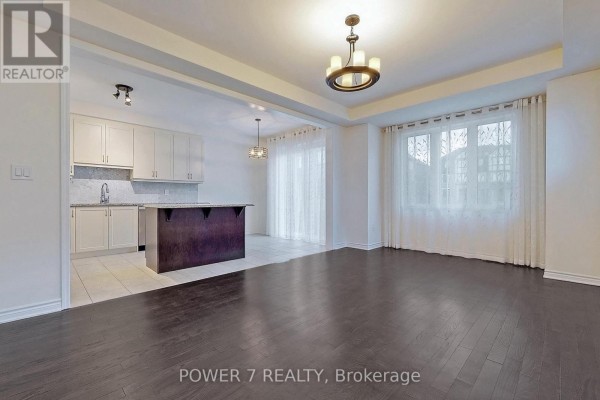 Open-concept living room with dark hardwood floors, white walls, and a kitchen with a dark island. - 41 Ness Drive, Richmond Hill