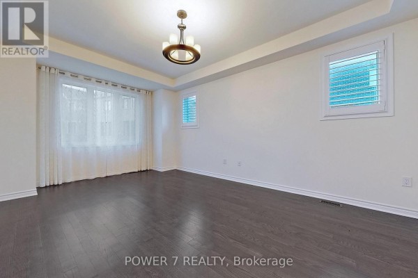 Spacious living room with dark hardwood floors, white walls, and white plantation shutters on windows. - 41 Ness Drive, Richmond Hill