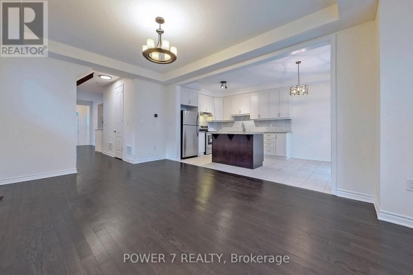 View of the open-concept living area flowing into the kitchen with stainless steel appliances and white cabinets. - 41 Ness Drive, Richmond Hill