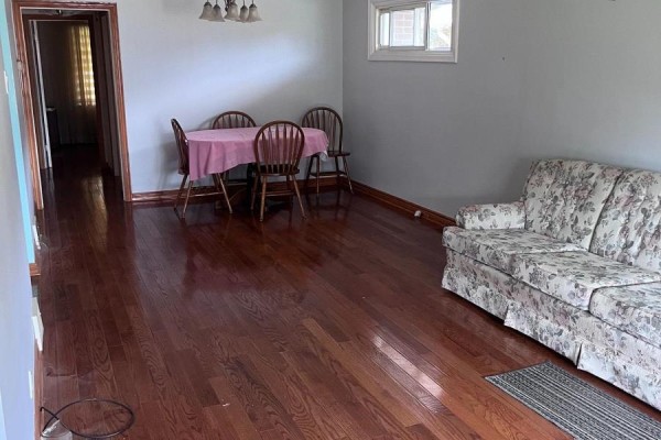 Living and dining room with polished hardwood floors, a floral sofa, and a round table with chairs. - 41 Pachino Boulevard, Toronto