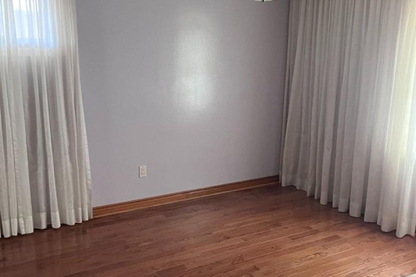 Empty room with polished hardwood floors and long white curtains covering two windows on opposite walls. - 41 Pachino Boulevard, Toronto