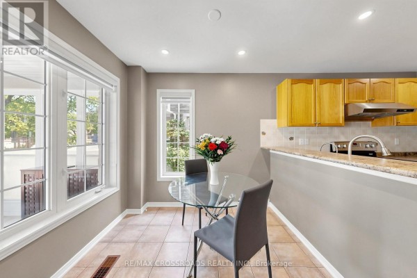 Dining area with a glass table, two dark chairs, beige tiled floor, and light brown cabinets. - 41 Prince Charles Way, Markham