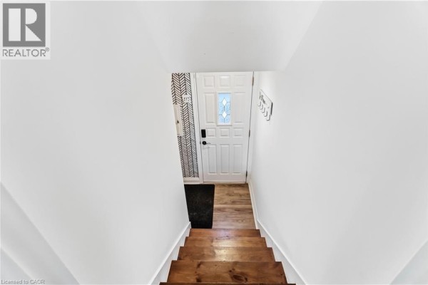 View looking down wooden stairs into a basement unit entrance with a white door. - 41 Sharon Avenue Unit# Basement Unit, Hamilton