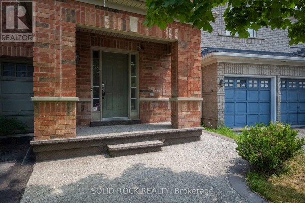 Close-up of the brick townhouse entrance with a covered porch and blue garage doors visible. - 41 Trumpet Valley Boulevard, Brampton