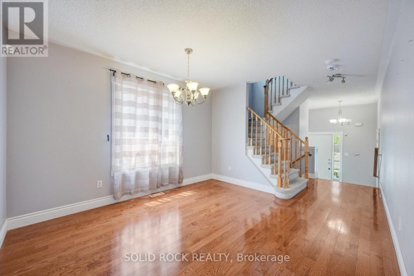 Living room with hardwood floors, large window with sheer curtains, and a staircase. - 41 Trumpet Valley Boulevard, Brampton