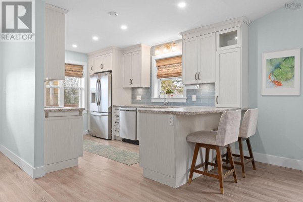 Modern kitchen with white cabinets, stainless steel appliances, and a breakfast bar with two stools. - 41 Wineberry Way, Upper Sackville