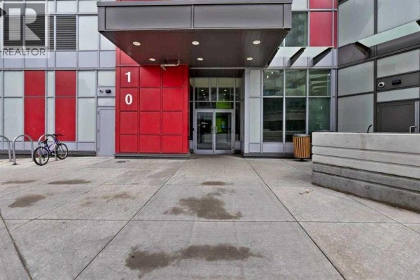 Entrance to apartment building with red and grey panels, glass doors, and concrete walkway. - 410, 10 Brentwood Common Nw, Calgary