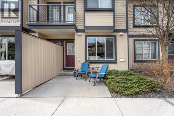 Close-up of townhouse entrance with two blue chairs and a small table on a concrete patio. - 410, 121 Copperpond Common Se, Calgary