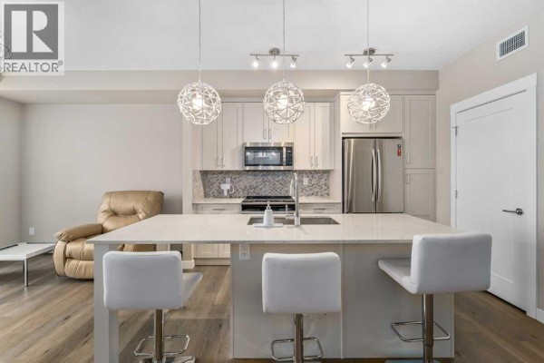Kitchen island with seating and a recliner chair in the living area. - 410, 35 Walgrove Walk Se, Calgary