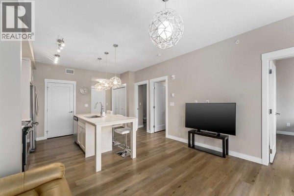 Open concept living and kitchen area with a large TV and multiple doors. - 410, 35 Walgrove Walk Se, Calgary
