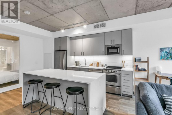 A modern kitchen with grey cabinets, stainless steel appliances, and an island with stools. - 410 - 115 Larchmount Avenue, Toronto
