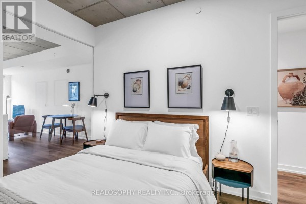 A bed with white linens, two nightstands, and artwork on the wall. - 410 - 115 Larchmount Avenue, Toronto