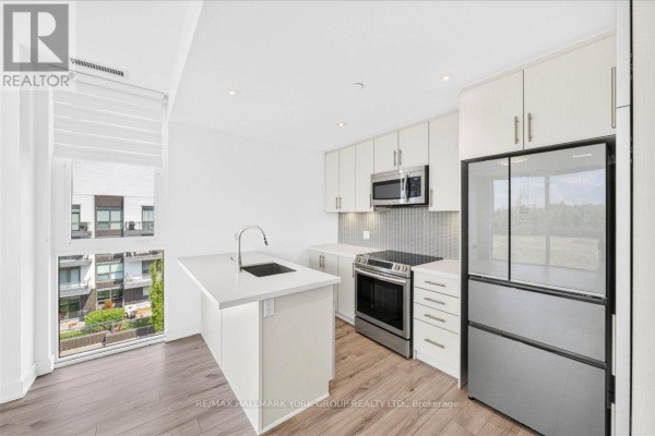 Modern white kitchen with stainless steel appliances, a central island with a sink, and a large window view. - 410 - 375 Sea Ray Avenue, Innisfil