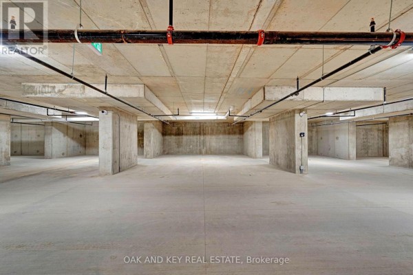 Empty concrete parking garage with exposed pipes and lighting. - 410 - 385 Hill Street, London East