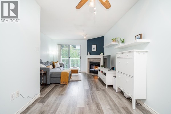Living room with light blue walls, a ceiling fan, and a fireplace, featuring laminate flooring. - 410 1035 Auckland Street, New Westminster