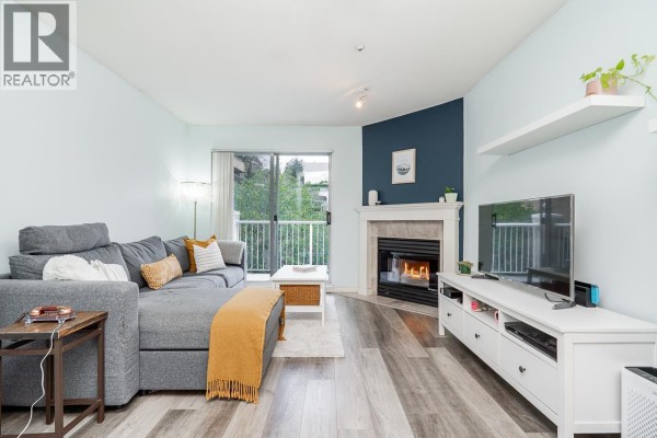 Cozy living room with a sectional sofa, fireplace, and access to a balcony with green views. - 410 1035 Auckland Street, New Westminster
