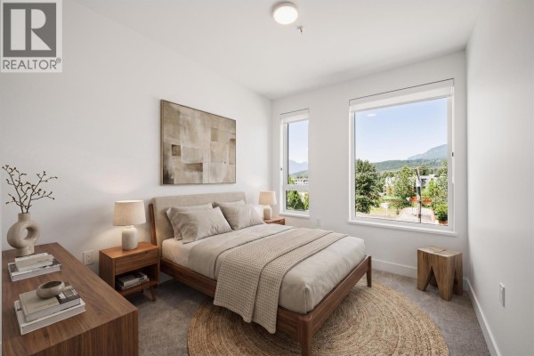 Bedroom with a queen-size bed, two nightstands, and windows overlooking a treed landscape. - 410 111 Buller Street, Port Moody