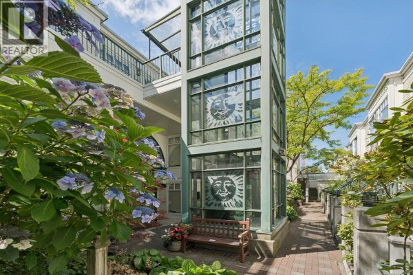 Outdoor walkway with a glass elevator shaft decorated with sun decals and plants. - 410 3727 W 10th Avenue, Vancouver