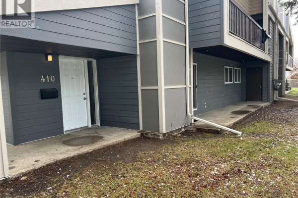 View of the building's exterior, showing the entrance and a sliding glass door with grey siding. - 410 510 Prairie Avenue, Saskatoon