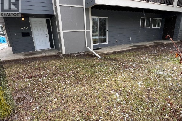 Ground-level view of the townhouse exterior with grass and falling snow, showing unit 410 entrance. - 410 510 Prairie Avenue, Saskatoon